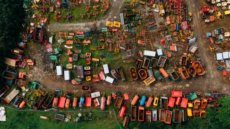 Aerial view of a large pile of mixed household waste and recyclable materials, including plastic bottles, cardboard, and paper, situated in an open dirt area adjacent to a paved road. The surrounding environment features dry, sparse vegetation along the edges of the waste pile, indicating a suburban or semi-rural location. It appears to be a waste disposal site or illegal dumping area, with no visible safety barriers or signage. The image highlights the need for proper waste management and recycling services, similar to those provided by Man with Van Leytonstone for responsible house removals and furniture transport, especially during home relocation and moving projects.