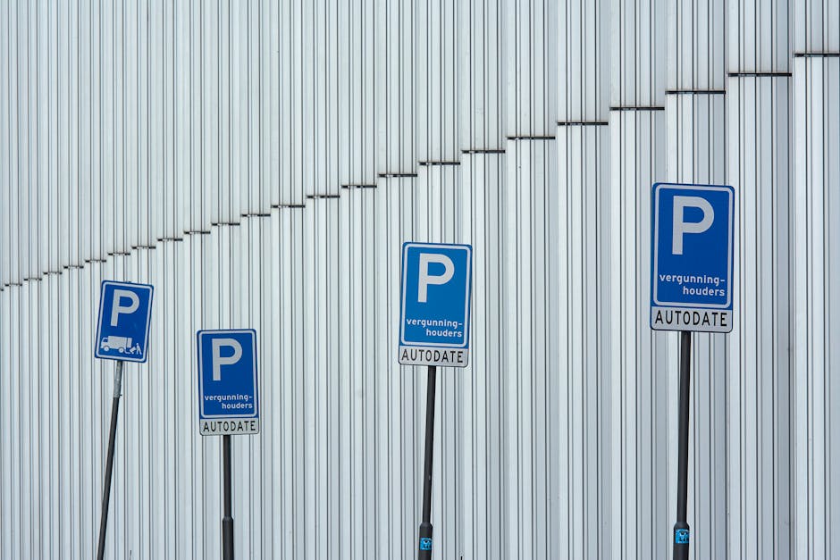 Four blue parking permit signs mounted on black metal posts stand in front of a tall, vertically paneled metallic wall. The signs display a large white 'P' with the words 'vergunning-houders' and 'AUTODATE' beneath, indicating parking permits for authorized vehicles. The signs are arranged in a row, with the tallest on the right and the shortest on the left, and are positioned on an urban pavement area. The lighting is natural, illuminating the signs and the textured metallic surface behind them. The image reflects aspects of parking management relevant to house removals and moving logistics, as provided by Man with Van Leytonstone, supporting the need for valid parking permits during home relocation or furniture transport in the Waltham Forest area.